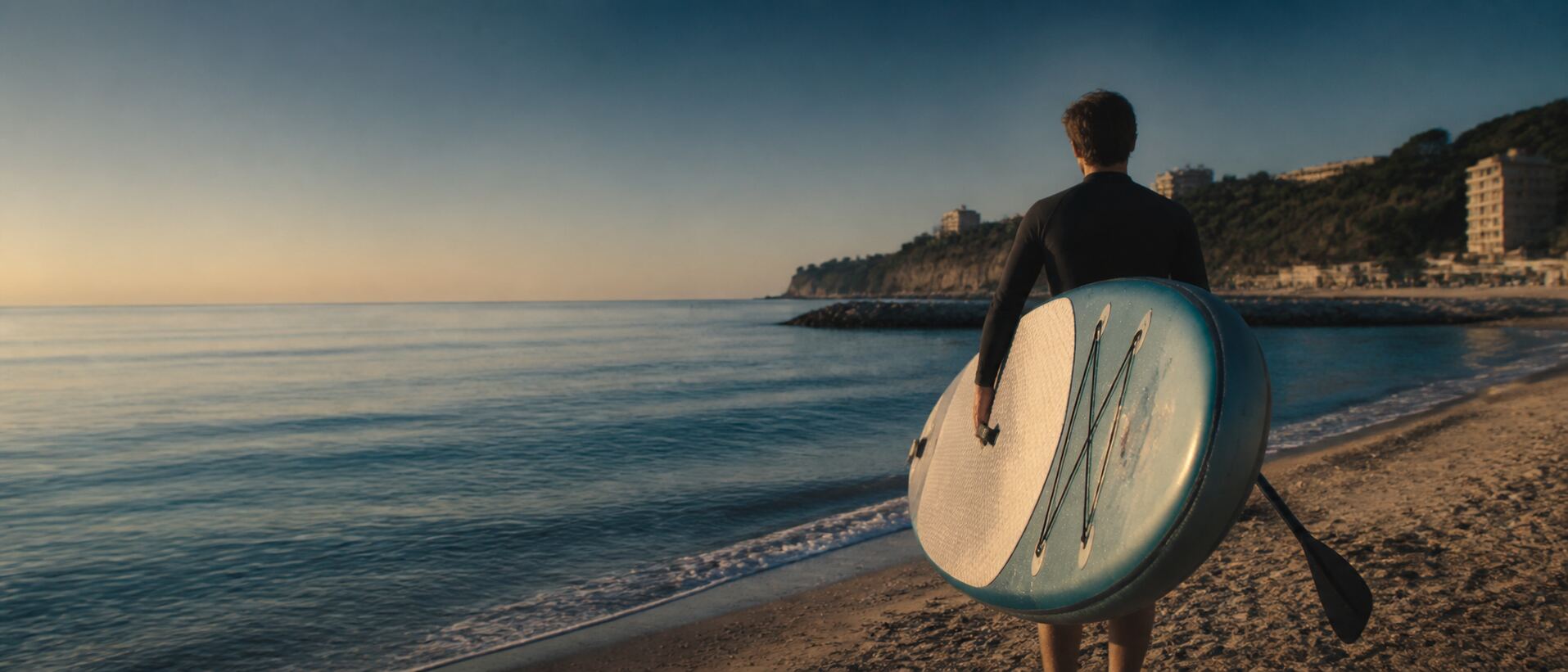 A person carrying their SUP towards the sea in the morning